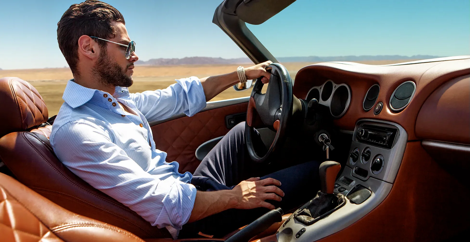 Photographie d'un homme en chemise et pantalon de costume roulant dans une voiture de luxe sur une route dans le désert