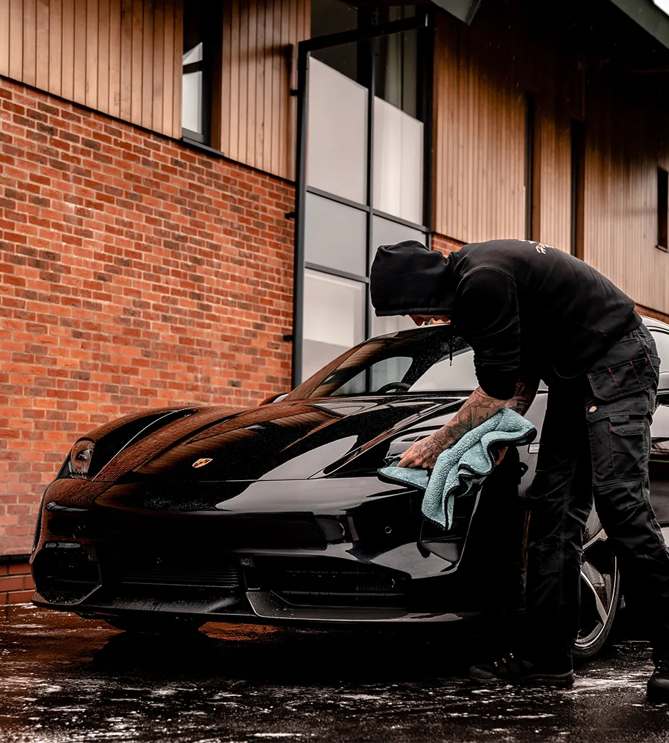 Photographie d'un homme nettoyant une voiture de luxe devant une maison